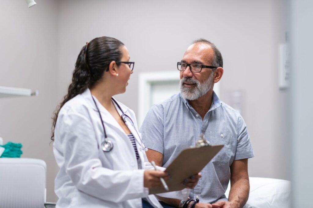 Female doctor talks with older adult man in office