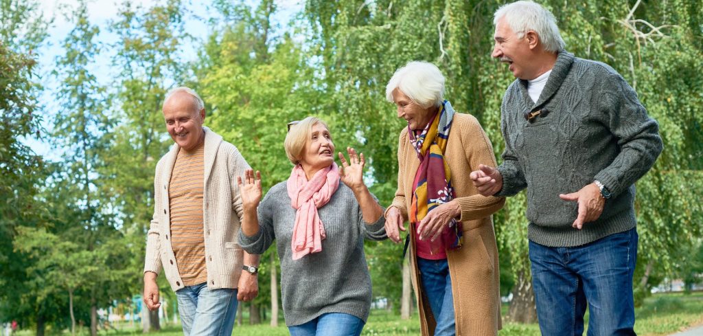 four older adults walking happily along a trail in a park