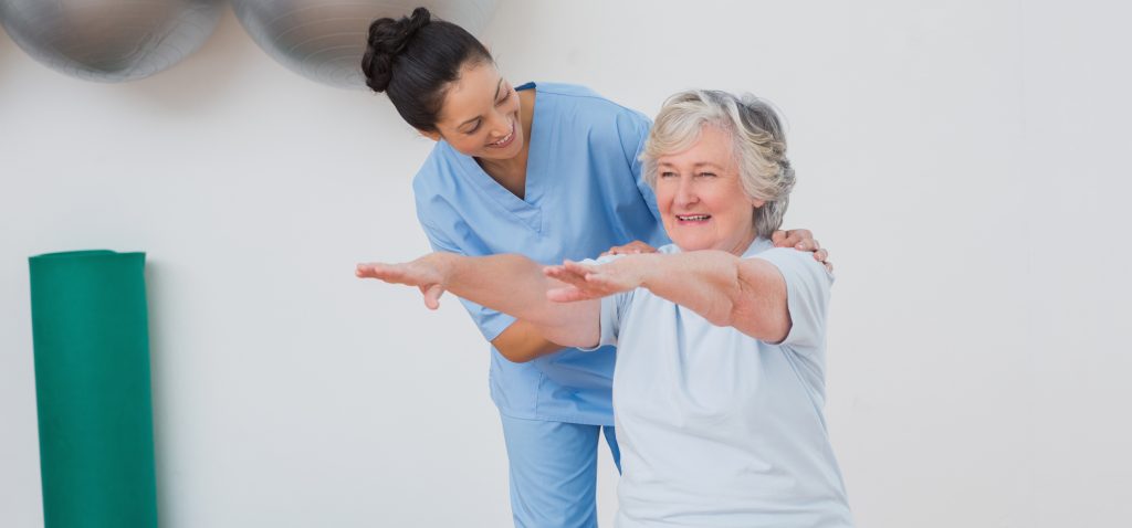 Happy instructor assisting older adult woman in exercising at gym