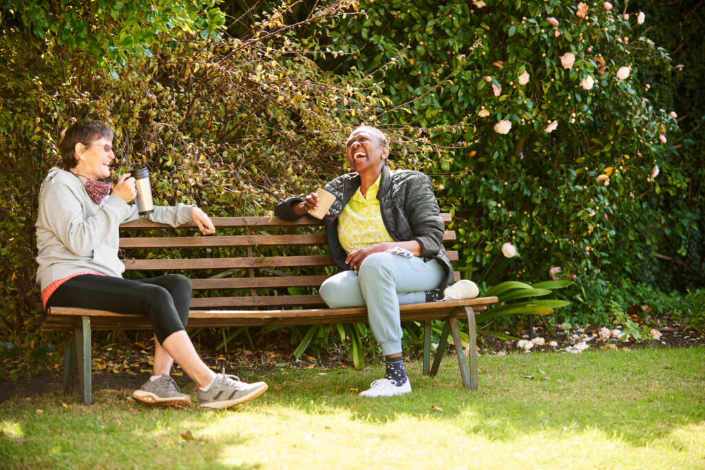 Two people drinking warm beverages while socialising on a bench